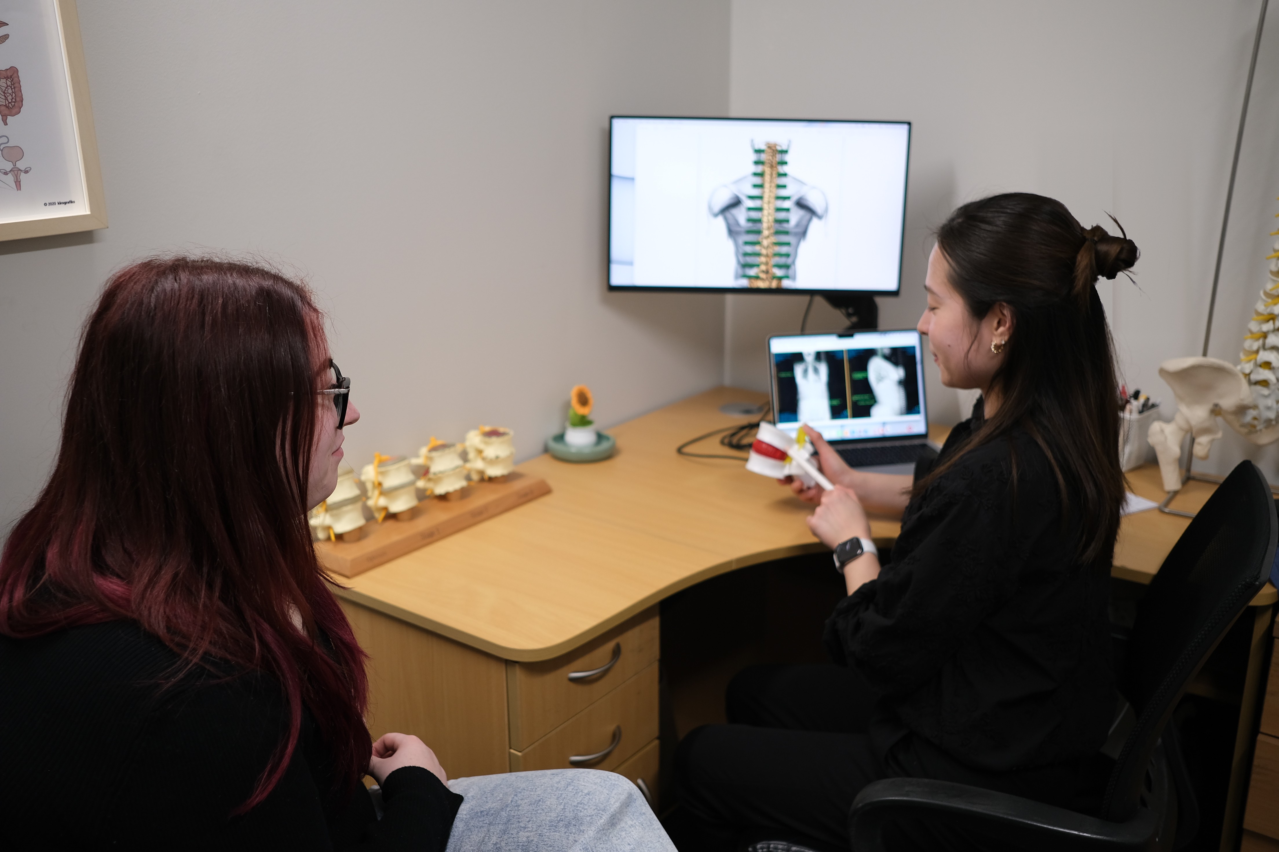 Chiropractor using a spine model and scans to explain findings to a patient at Langford Chiropractic